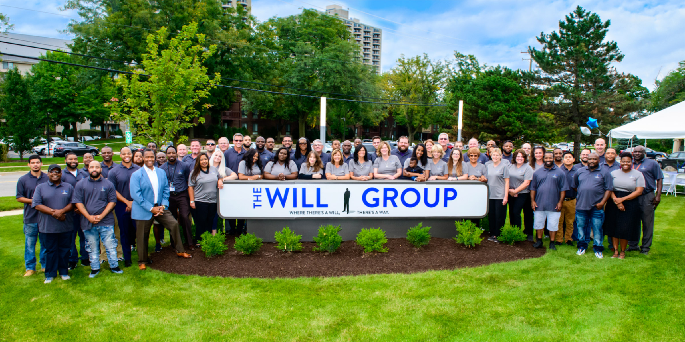 Group photo of The Will Group staff standing around the company sign